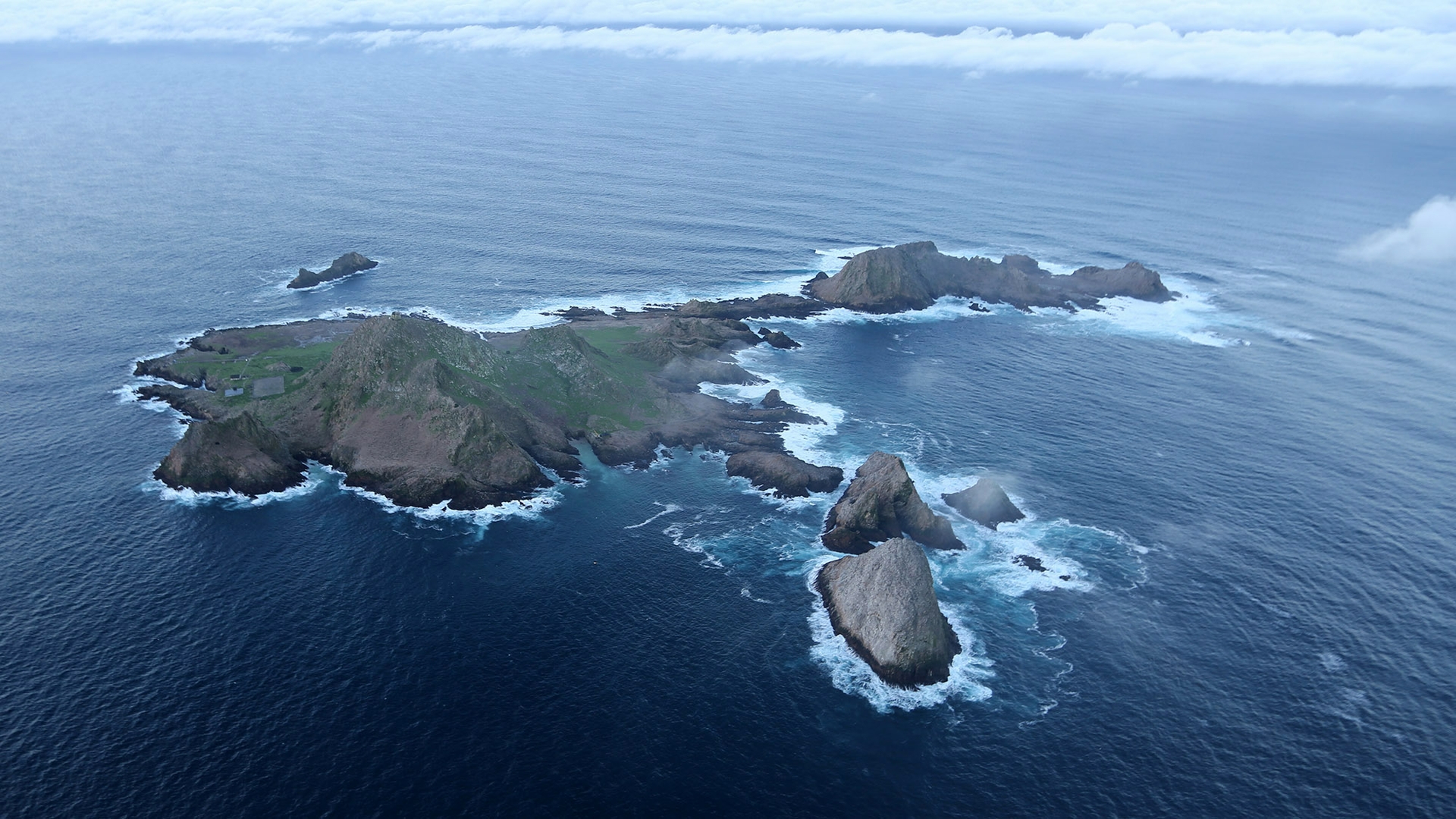 Aerial image of Southeast Farallon Island; the rocky main island of the Farallon Islands surrounded by blue water with clouds on the horizon.